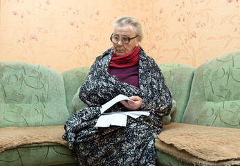 An elderly woman looks at utility bills.