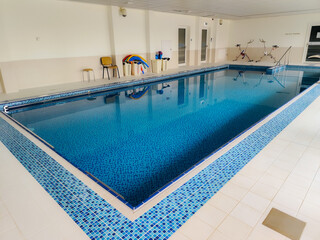 Clean indoor swimming pool with blue mosaic tiles, stainless steel handrails, and shallow entry steps, designed for training, therapy, or leisure.