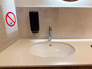 Bathroom sink with faucet, soap dispenser and no smoking sign on wall. Hygiene, facility, and modern design highlighting cleanliness, caution, and sanitary routine.