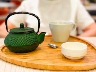 Green cast iron teapot with cup and spoon on wooden tray. Beverage, hospitality, and lifestyle highlighting tradition, refreshment, and cultural dining ritual.