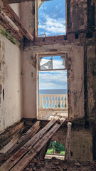Fototapeta premium Inside a decaying historic building with broken windows, overlooking the clear blue sea. Architecture in ruin, concept of abandonment.