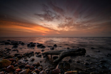 Obraz premium Stunning sunset over the Baltic Sea, capturing the warm golden hues reflecting on calm water. Serene coastal landscape with peaceful waves and a colorful sky