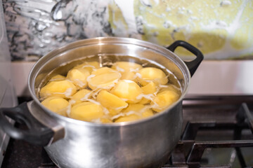 Peeled potatoes are boiled in a stainless steel pot on a gas stove.