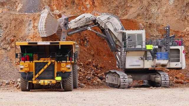 Excavator loads copper ore into big dump truck in open gold pit mine. Process gold mining industry workplace.