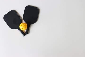 Black pickleball paddle and ball in a light backgroundWith copy space in the righ side
