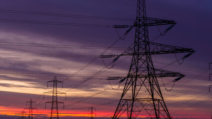 Electricity Pylons Against Vibrant Sunrise in a Rural Landscape
