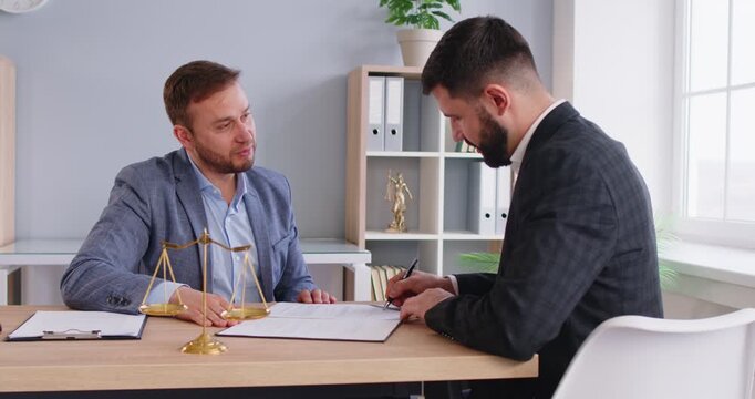 Cheerful male lawyer make a deal shaking hand with man client sitting at the desk on workplace in office signing documents. Legal law and advice concept. 4k video. Slow motion video.