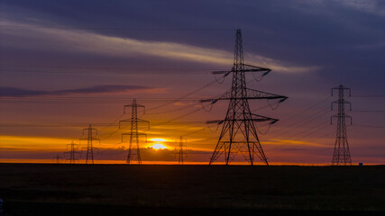 Electricity Pylons at Sunrise Across a Remote Countryside Landscape