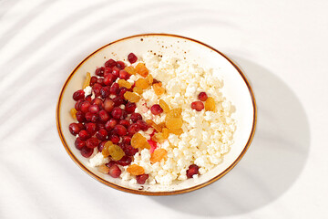 Granular fresh cottage cheese with pomegranate seeds and raisins on a sunny table, natural nutrition concept, healthy lifestyle advertising, baby food. Healthy breakfast with ingredients,