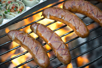 Juicy sausages grilling on a barbecue in the garden. Summer outdoor gathering, traditional food, smoky flavor, and festive picnic atmosphere.
