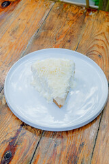 Delicious slice of cake with white frosting and cheese on a white plate, ready to eat