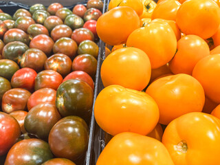 Fresh tomatoes in vibrant colors, red and orange varieties displayed in a market setting, showcasing the abundance of produce and inviting atmosphere for healthy eating