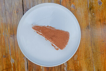 Indulge in delicious tiramisu cake artfully presented on a modern white plate, resting on rustic wooden table