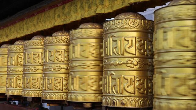 Rotating brass prayer wheels in Nepal monastery. Buddhist symbols, mantra engraving, spinning motion, cultural heritage, traditional ritual, spiritual architecture