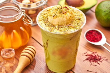 Creamy Avocado Smoothie with a Scoop of Ice Cream, Saffron, honey and Pistachio Crumble in plastic cup side view of summer drink