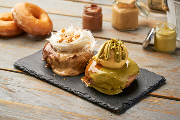 Donuts with Chocolate and Pistachio Glazed with Vanilla Ice Cream and Toppings on dark slate on a Wooden Table side view of indulgent dessert
