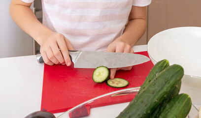 Cropped shot of girl cutting cucumber with knife on a table in kitchen