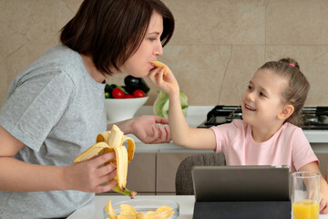 Daughter feeding mother with potato chips in kitchen
