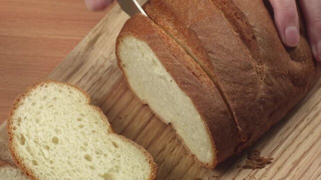Close-up of young woman slicing fresh white bread with a kitchen knife on a cutting board in her kitchen, recorded with ambient sound.