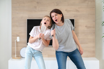 Happy family young adult mother and cute teen daughter having fun singing karaoke song in hairbrushes. mother laughing enjoying funny lifestyle activity with teenage girl at home together.