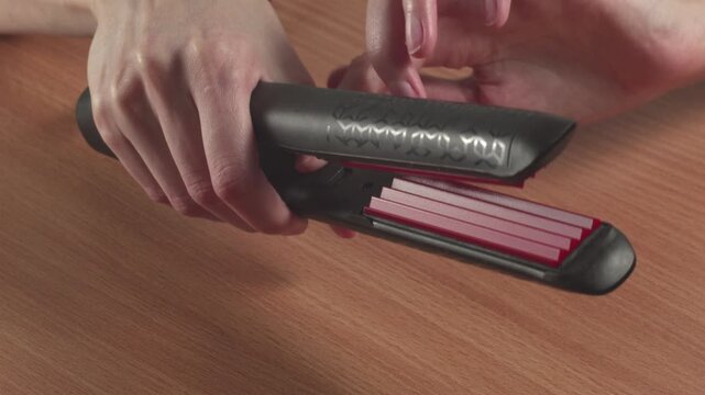 Close-up of woman using a hair curling iron at home, recorded with ambient sound.