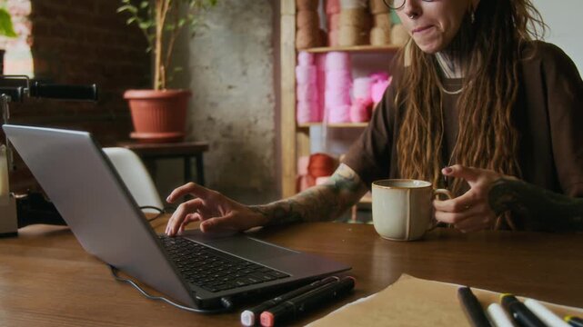 Close up shot of creative young woman using laptop in workshop with focus on tattooed hands typing, copy space