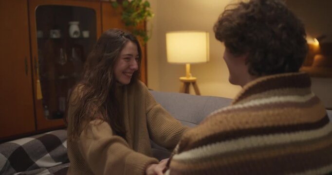 Over the shoulder teenage girl laughs and gets embarrassed as she kisses her boyfriend on the cheek during a cozy evening of chatting at home. Young Adult Romance