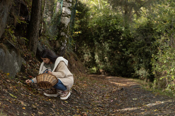 Mujer recolectando setas en el bosque con cesta de mimbre durante el otoño