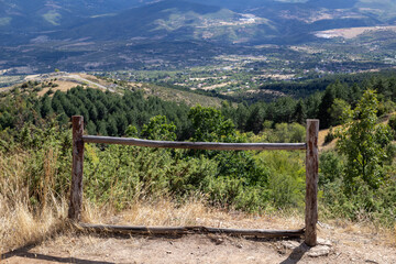 sprawling mountain landscape, framed by a rustic wooden fence in the foreground, creating a sense...