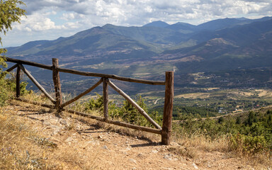 sprawling mountain landscape, framed by a rustic wooden fence in the foreground, creating a sense...