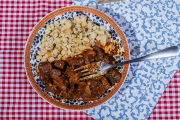 Hungarian goulash with spaetzle on checkered tablecloth: delicious traditional stew