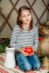 Little girl with an apple on a striped blanket near a basket of flowers and jug of milk.