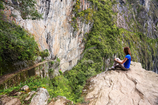 Young woman enjoying the view of Inca Bridge and cliff path near Machu Picchu in Peru