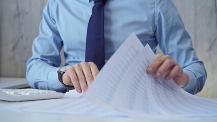 Businessman accountant with blue t-shirt is calculating numbers for a financial audit and taking notes with a silver pen. Taxes and audit concept