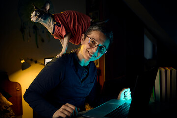 Woman typing on laptop with Sphynx cat climbing on her shoulder