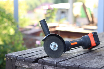 Cordless grinder lies on a wooden surface, close-up. Repair at the cottage or construction. Working tool. Compact cordless angle grinder. Power tools. DIY repair concept, construction equipment