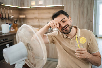 Man refreshing himself with a fan and a cold drink during a heat wave