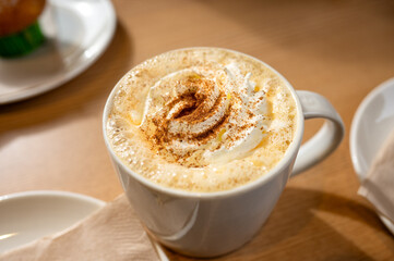 Freshly made pumpkin spice latte coffee with cream served in a white mug on a wooden cafe table. High quality photo