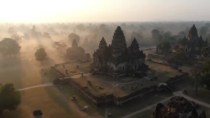 Sunrise over ancient angkor wat temple complex in cambodia, shrouded in mist, with sunbeams illuminating the iconic towers and surrounding jungle - Powered by Adobe