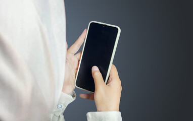Hijab-wearing Woman Holding Smartphone, Interacting with Modern Technology on Dark Background