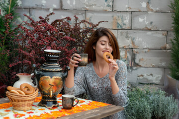 Young smiling woman in sweater drinking tea with bun in autumn garden. Autumn seasonal gardening, hobby and weekend concept. Selective focus