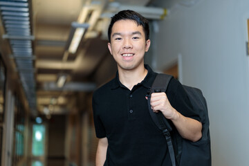 A young man stands confidently in a university hallway with a backpack over one shoulder. He appears ready for class or study on campus. © fotolite