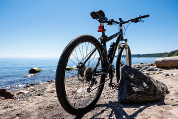 Fototapeta premium Rear view of mountain bike on the beach with water and lake background, showing detailed rear wheel, derailleur, and chain