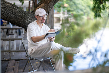 man is sitting on a chair and writing in a notebook