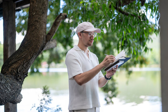 man is writing in a notebook while standing in front of a tree