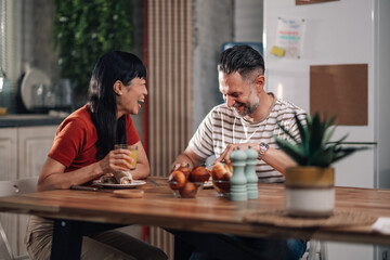 Happy couple enjoying breakfast and laughing together at home