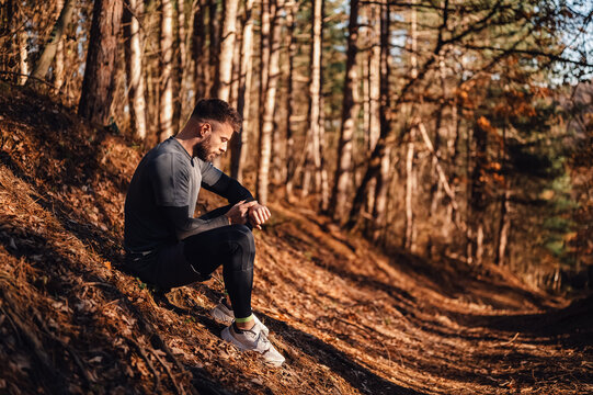 Male runner checking smartwatch on forest trail during golden hour - Powered by Adobe