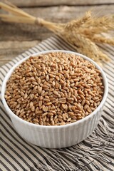 Wheat grains in bowl and spikes on wooden table, closeup