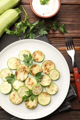 Delicious fried courgette slices with parsley served on wooden table, flat lay