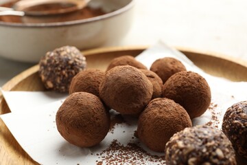 Tasty chocolate candies with cocoa powder on light table, closeup